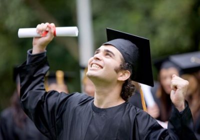 A proud graduate holds his degree and smiles towards the sky